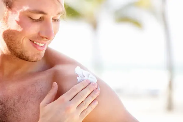 Junger Mann cremt sich am Strand mit Sonnenschutz ein