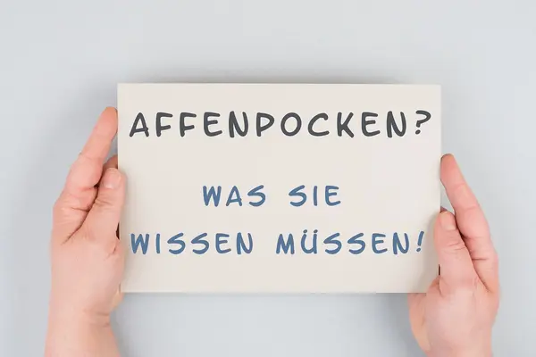 Ein Schild wird festgehalten. Es hat die Aufschrift "Affenpocken? Was Sie wissen müssen!".
