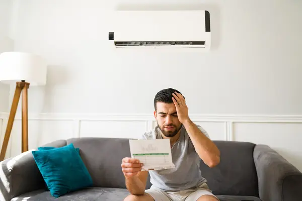 Mann sitzt auf dem Sofa und schaut auf seine hohe Stromrechnung