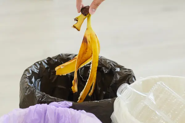 Hand wirft Bananenschale in den Abfall