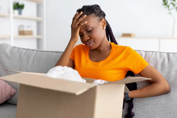 Eine junge Frau sitzt auf dem Sofa mit einem geöffneten Paket auf dem Schoß.