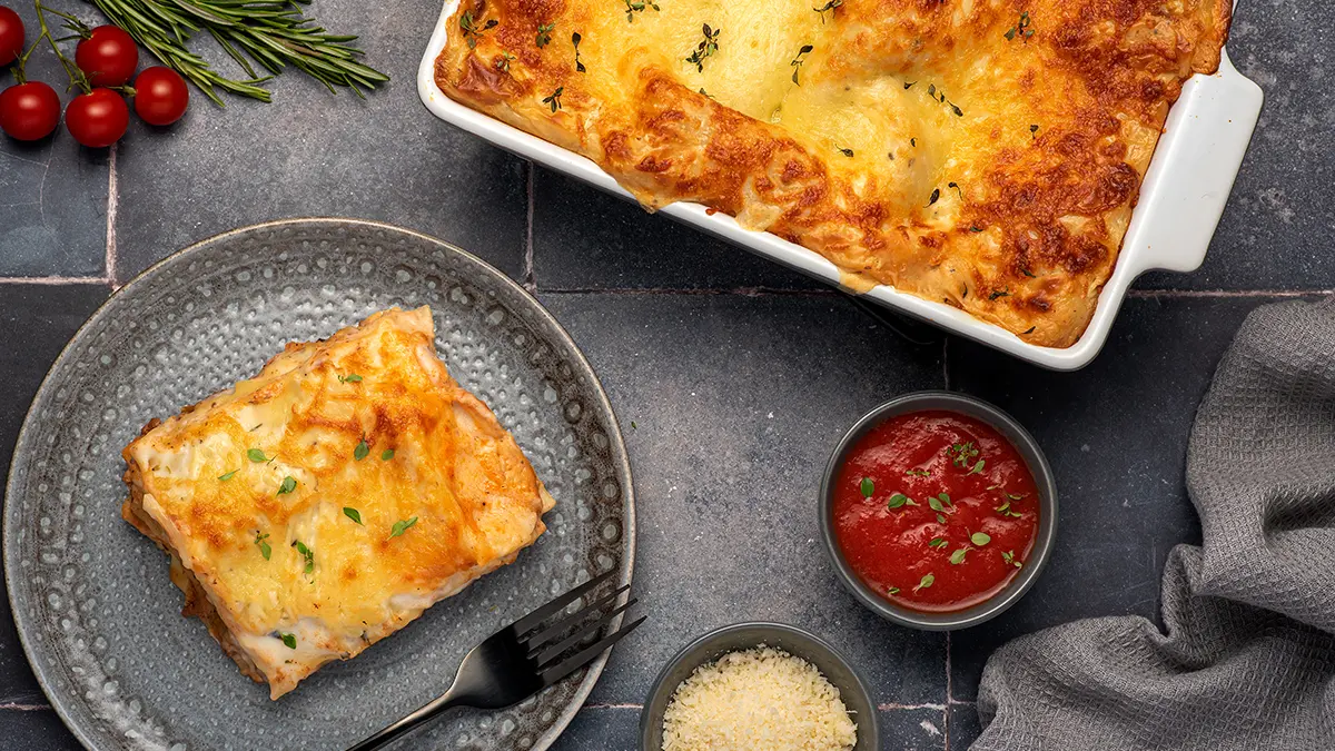 Lasagne in einer Auflaufform, ein Stück auf einem Teller.