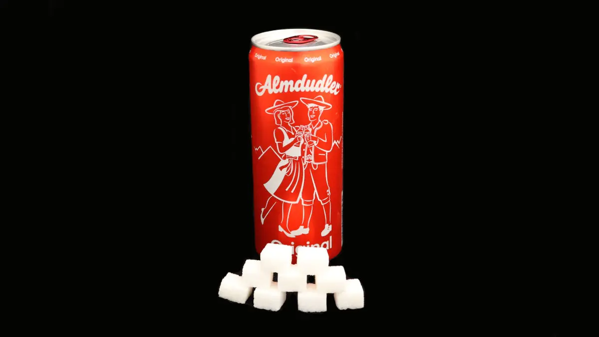 Dose Almdudler auf schwarzem Grund mit 9 Zuckerwürfeln davor