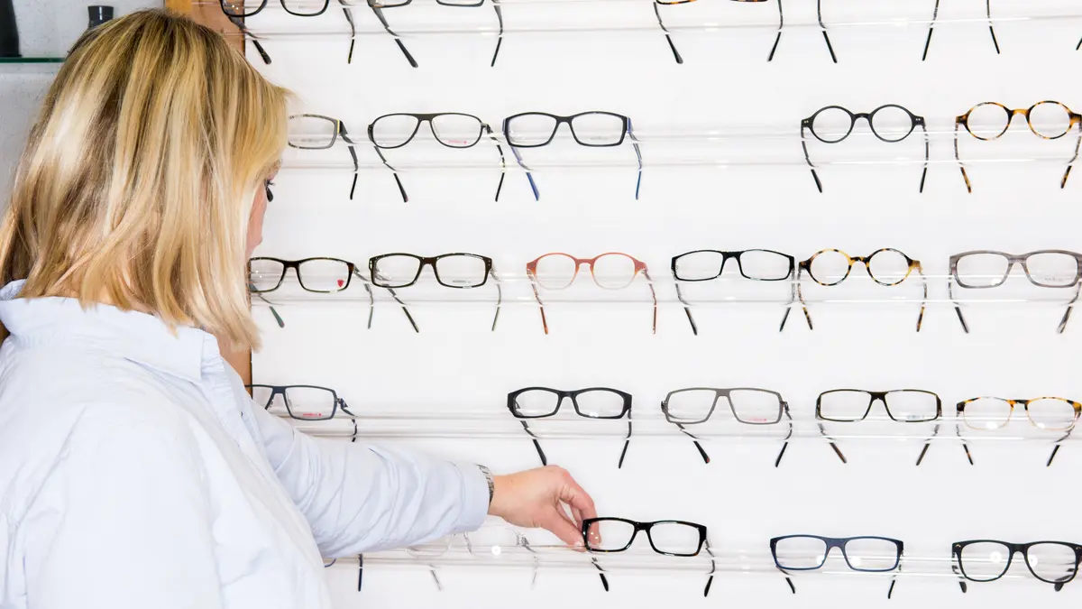 Eine Frau steht beim Optiker vor einer großen Auswahl an Brillen.