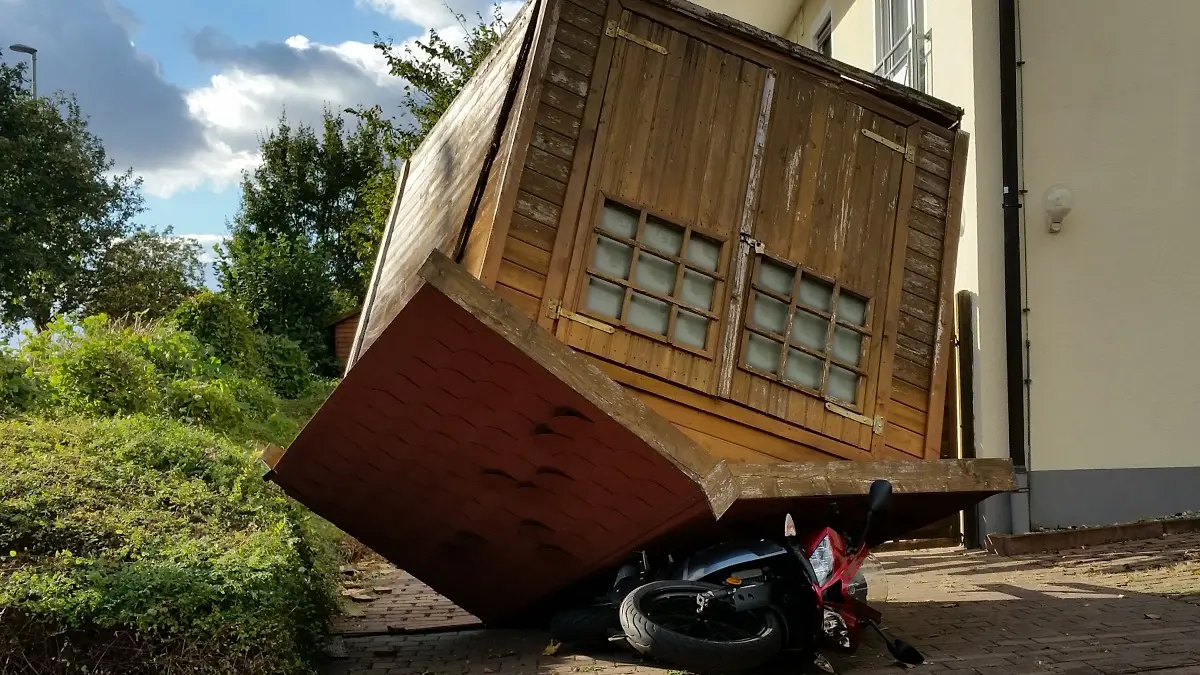 Ein Gartenhaus liegt auf dem Dach udn hat unter sich ein Motorrad begraben.