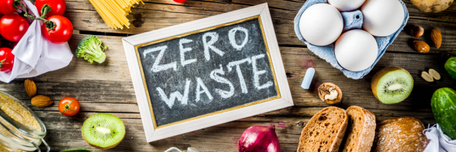 Ein Schildchen mit der Aufschrift "Zero Waste" liegt zwischen Lebensmittel auf einem Tisch.