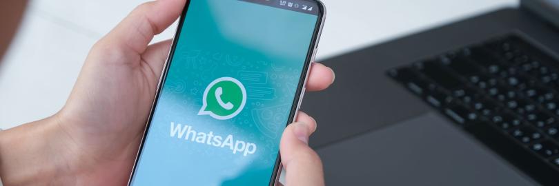 Jemand hält ein Handy in der Hand, auf dessen Display das WhatsApp-Logo zu sehen ist
