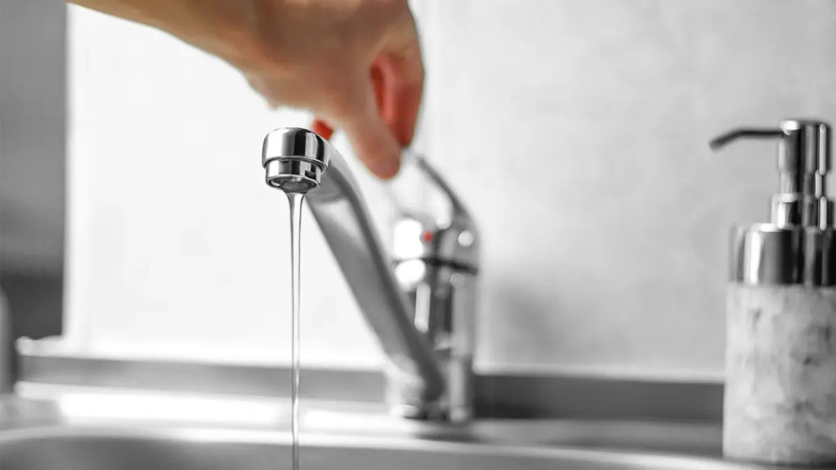 Hand öffnet einen Wasserhahn in eine Badezimmer
