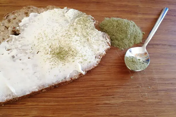 Eine Scheibe Brot, mit Frischkäse und Schabzigerklee als Gewürz darauf liegt auf einem Tisch.