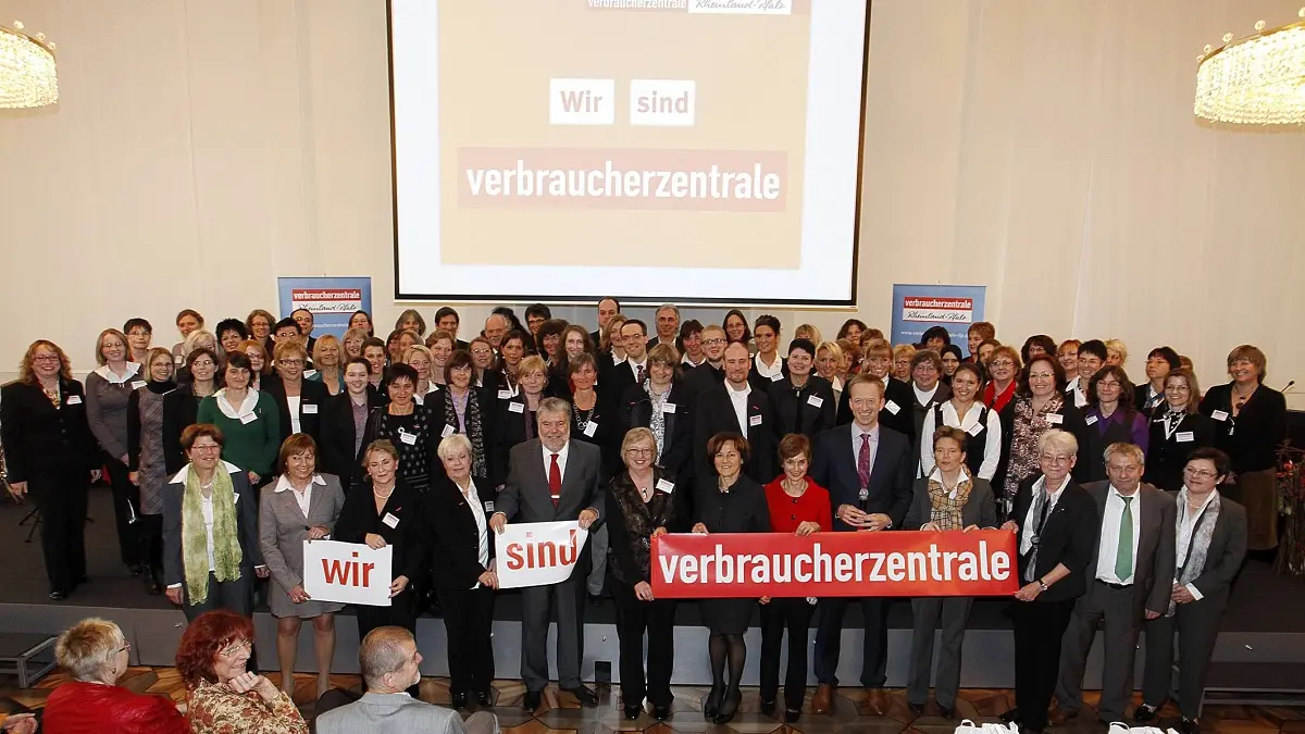 Viele Menschen auf eienr Bühne, die in die Kamera blicken und ein Schild vor sich halten.