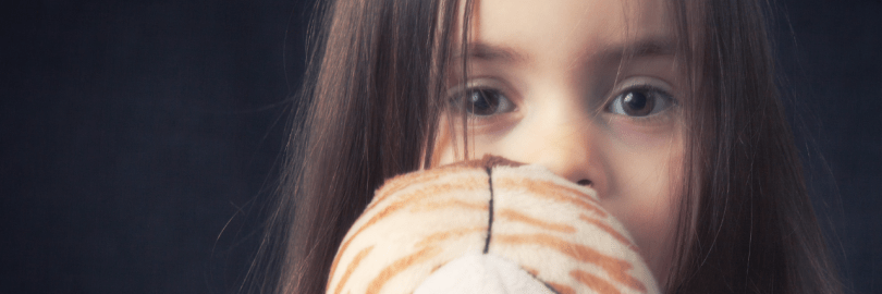 Ein verängstigtes Kind hält ein Kuscheltier vor das Gesicht.