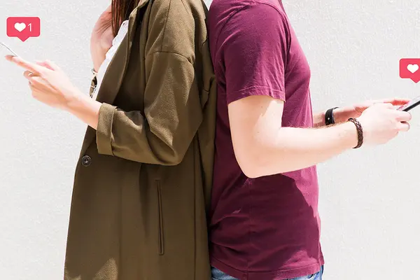 Ein Paar steht Rücken an Rücken, beide halten Smartphones und kommunizieren über eine Dating-App