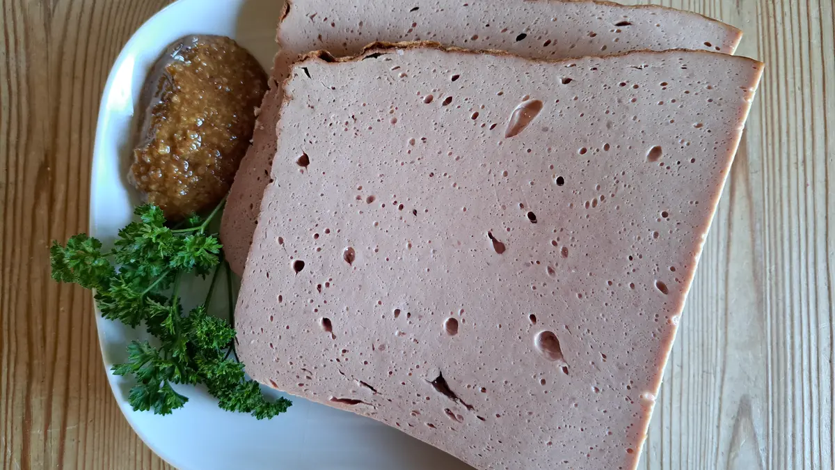 Zwei Scheiben Leberkäse liegen auf einem weißen Teller; daneben süßer Senf un Petersilie