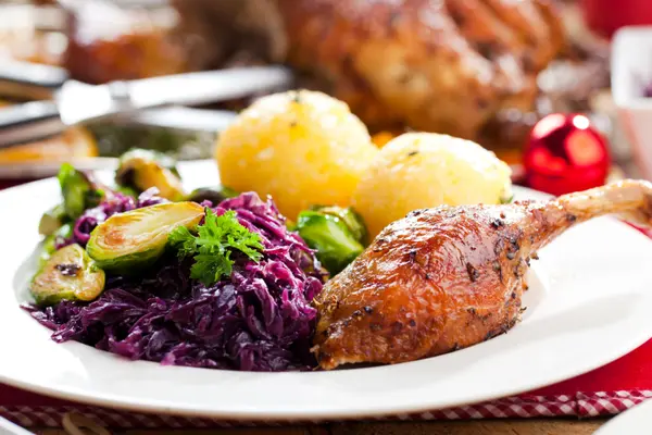 Auf einem Festtagstisch steht ein Teller mit Enten-Keule, Knödeln und Rotkohl