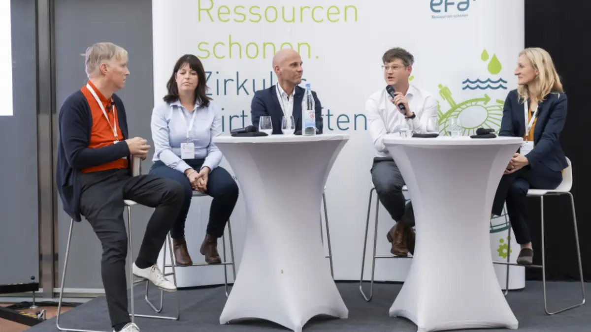 5 Leute an Tischen bei Diskussion auf demPosium