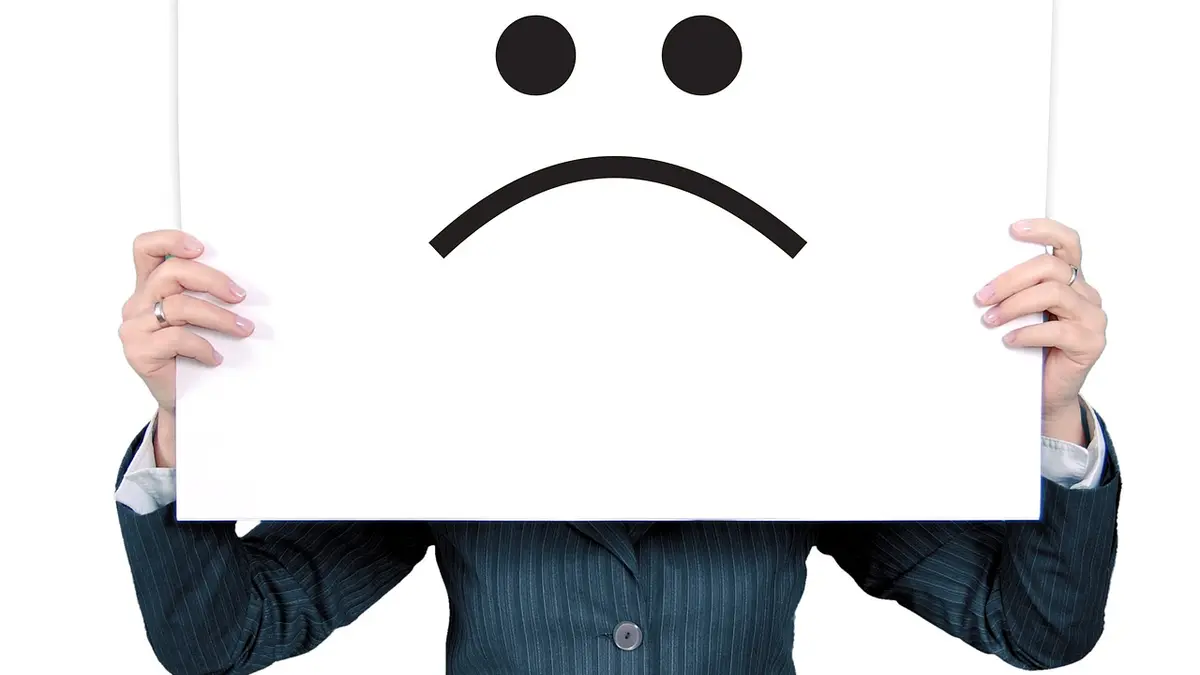 Frau hält großes Plakat mit einem Ärger-Emoticon vor ihr Gesicht