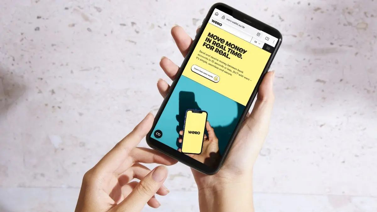 Zwei Hände halten ein Smartphone, auf dem Display ist die Internetseite von Wero zu sehen