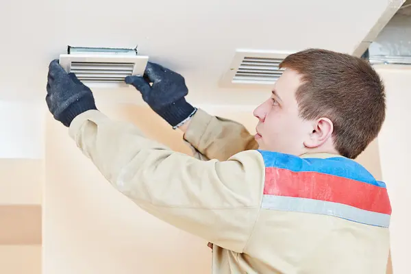 Installateur arbeitet an Lüftungsöffnung an einer Decke