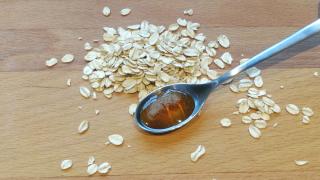 Ein Löffel mit Hafersirup liegt auf einem Holztisch, daneben liegen Haferflocken