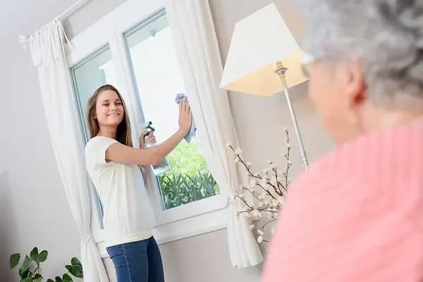 Putzkraft beim Reinigen der Fenster einer Seniorin
