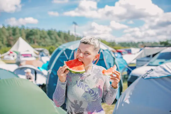 JUnge Frau isst Melone vor einer Zeltlandschaft