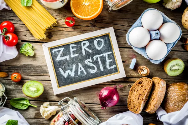 Ein Schildchen mit der Aufschrift "Zero Waste" liegt zwischen Lebensmittel auf einem Tisch.