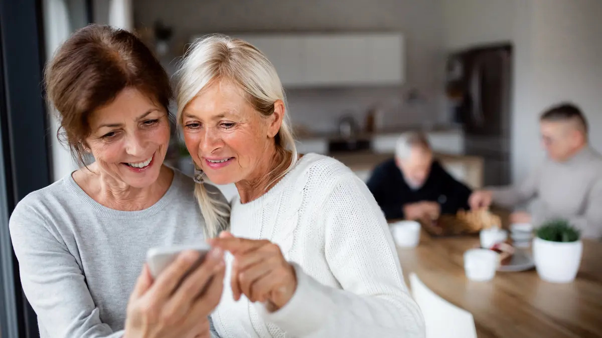 Zwei sportlich wirkende Frauen um die 70 schauen in der Küche gemeinsam auf ein Smartphone