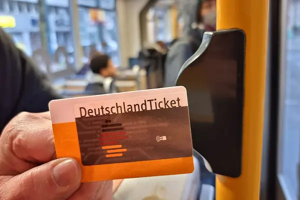 Eine Hand hält ein Deutschlandticket neben einen Stopp-Knopf an der Tür einer Straßenbahn
