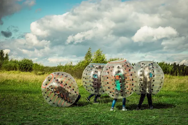 Jugendliche spielen auf einer Wiese in großen aufblasbaren Gummibällen (Bumperballs)  