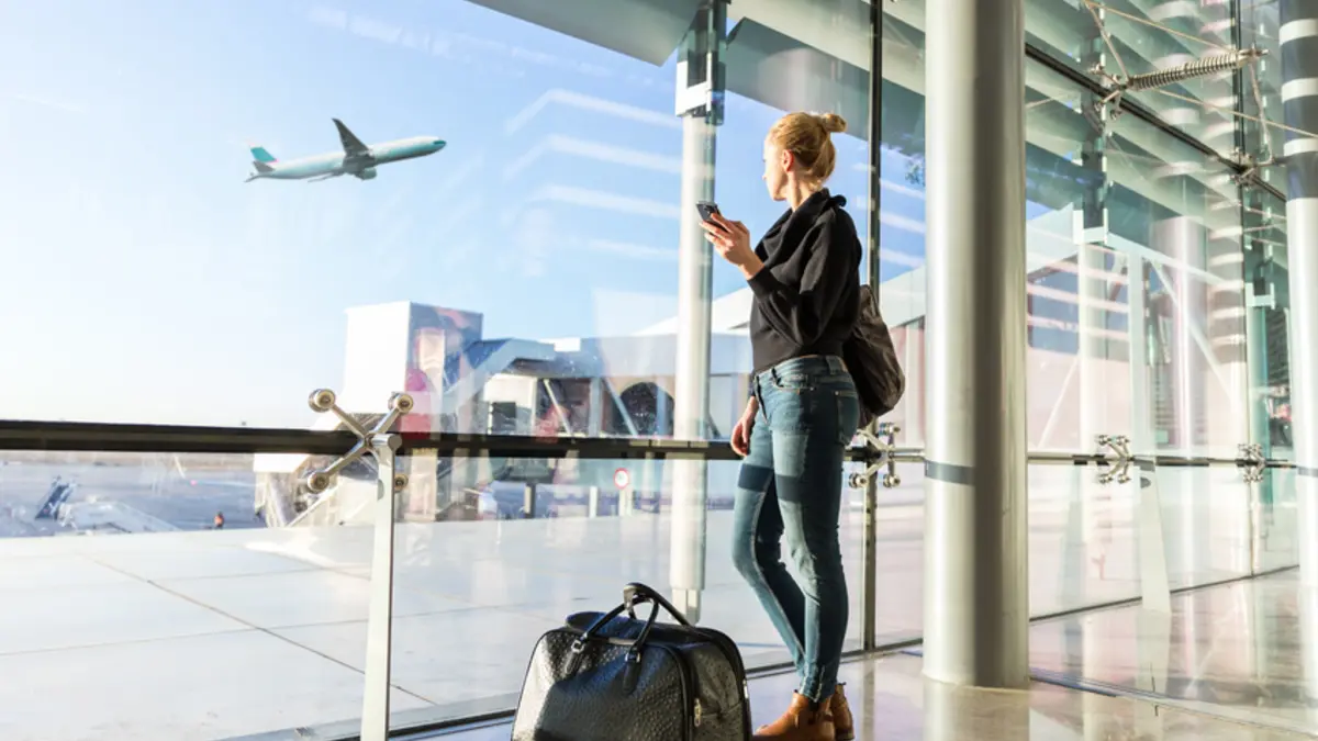 Frau schaut am Flughafen auf startendes Flugzeug