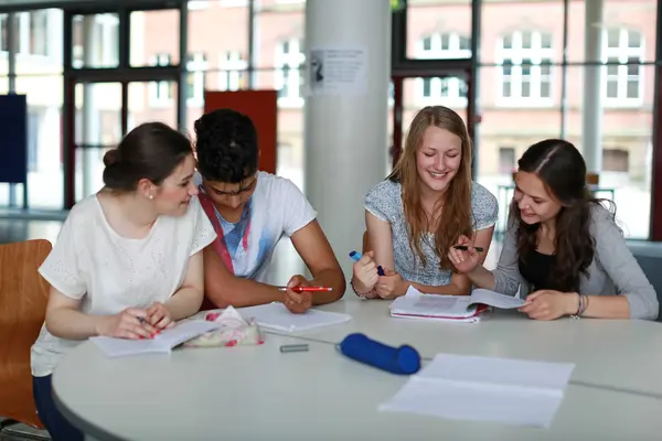 Vier Schüler*innen sitzen an einem Tisch und lernen gemeinsam