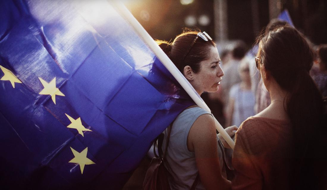  Zwei Personen stehen zusammen; eine von ihnen hält eine große EU-Flagge in der Hand