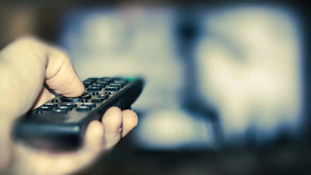 Jemand schaltet den Fernseher über die Fernbedienung an.