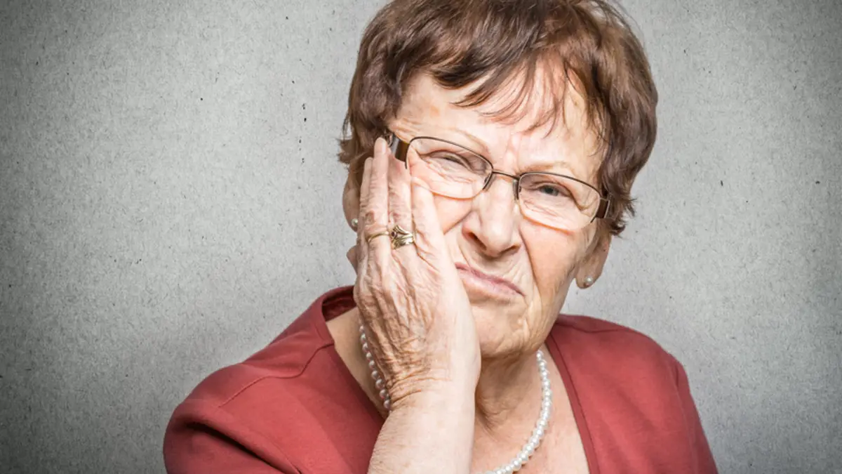 Seniorin hält sich die Wange, weil ihr Zahnersatz Beschwerden verursacht.
