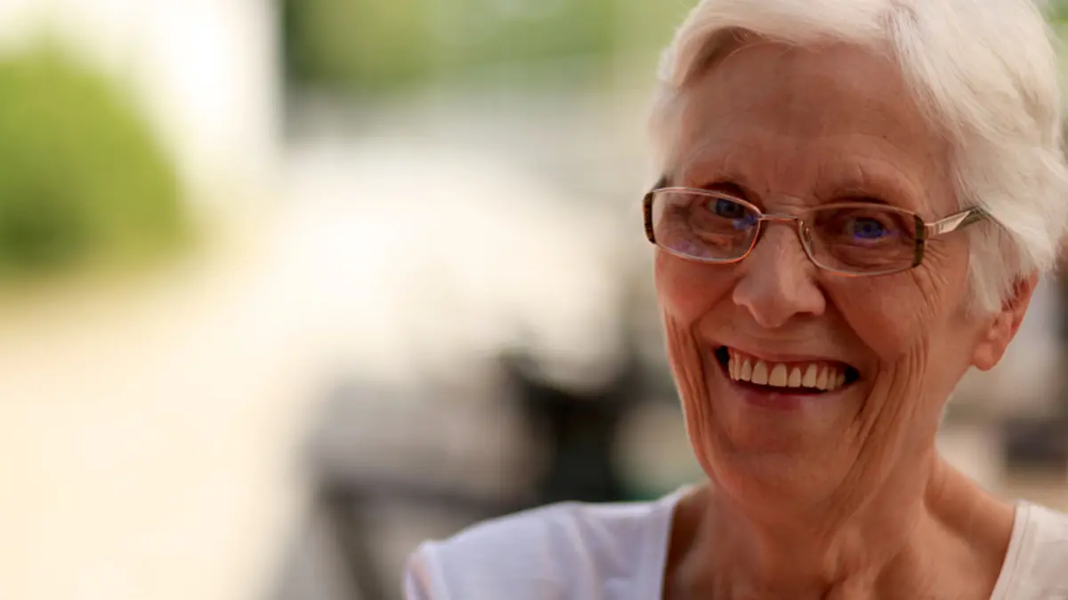 Seniorin lächelt zufrieden und zeigt dabei ihre schönen dritten Zähne (Zahnersatz).