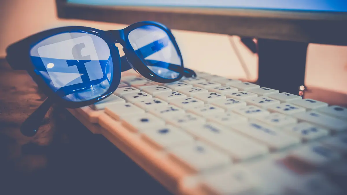 Auf einer Computertastatur liegt eine Brille, in der sich das Facebook-Logo spiegelt.