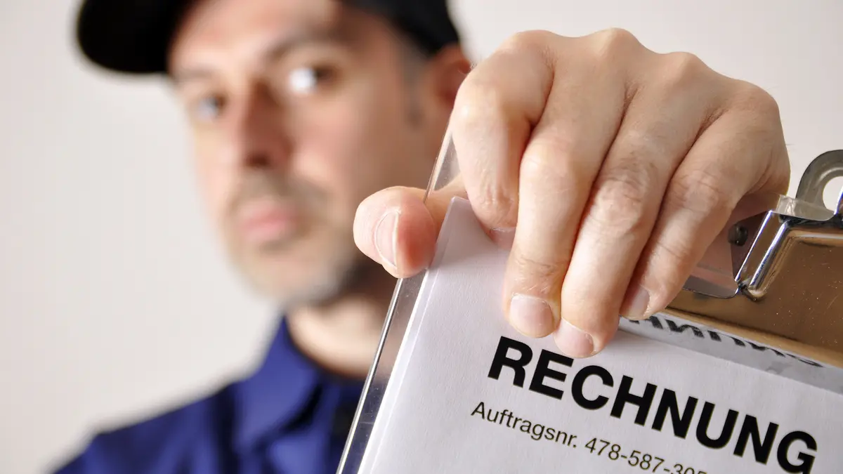 Ein Handwerker hält eine Rechnung in die Kamera