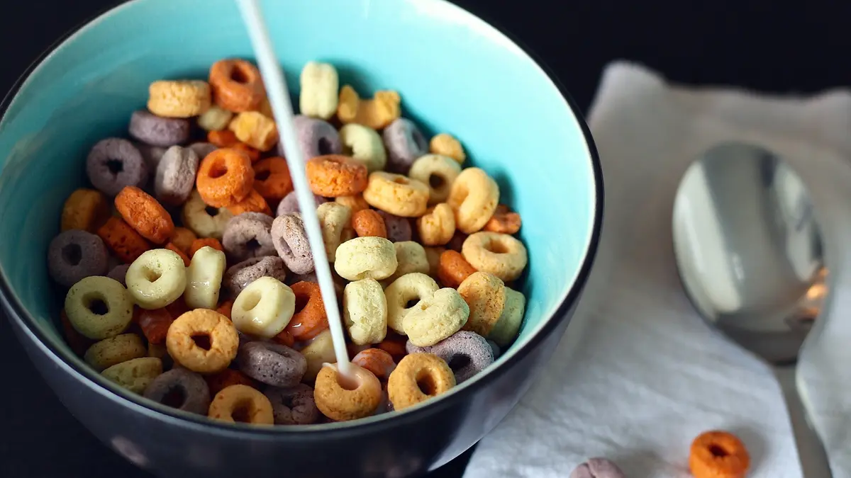 Schüssel mit bunten Frühstücksflocken, in die Milch eingegossen wird.