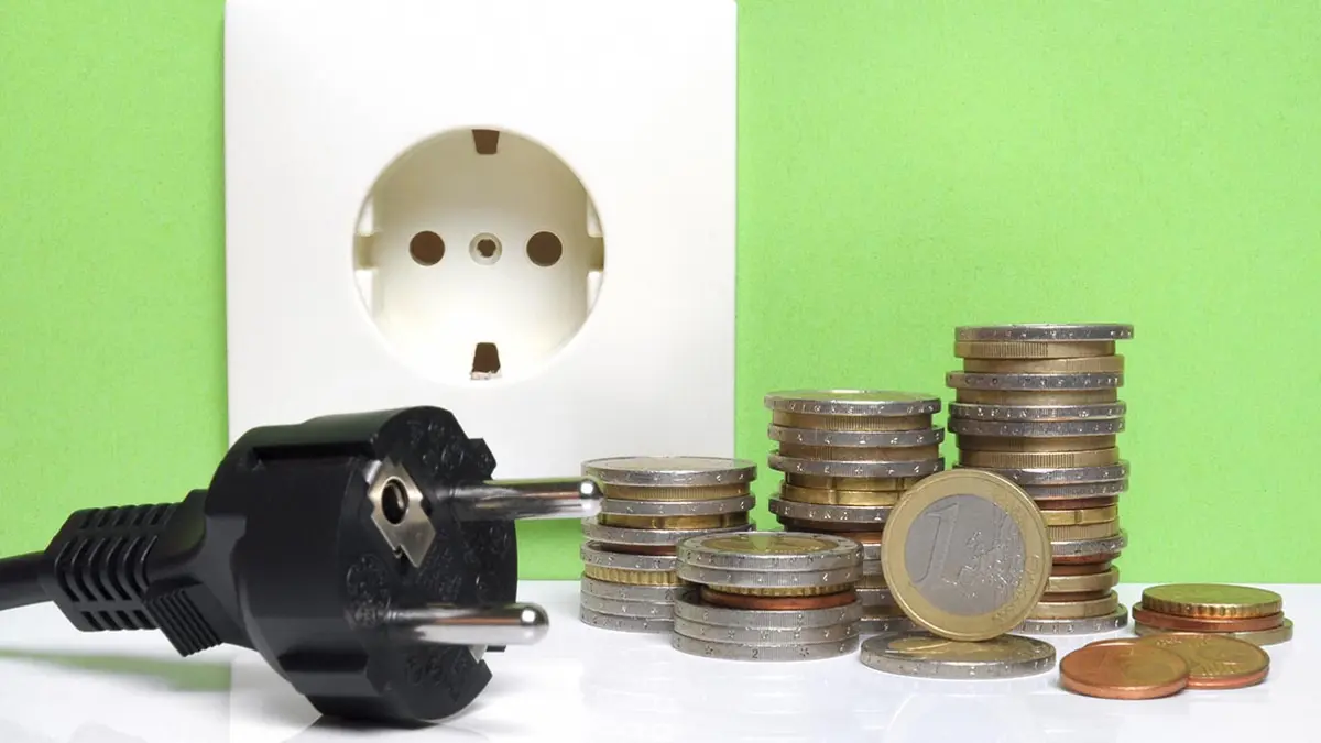 Stromstecker und Münzen liegen vor einer Steckdose
