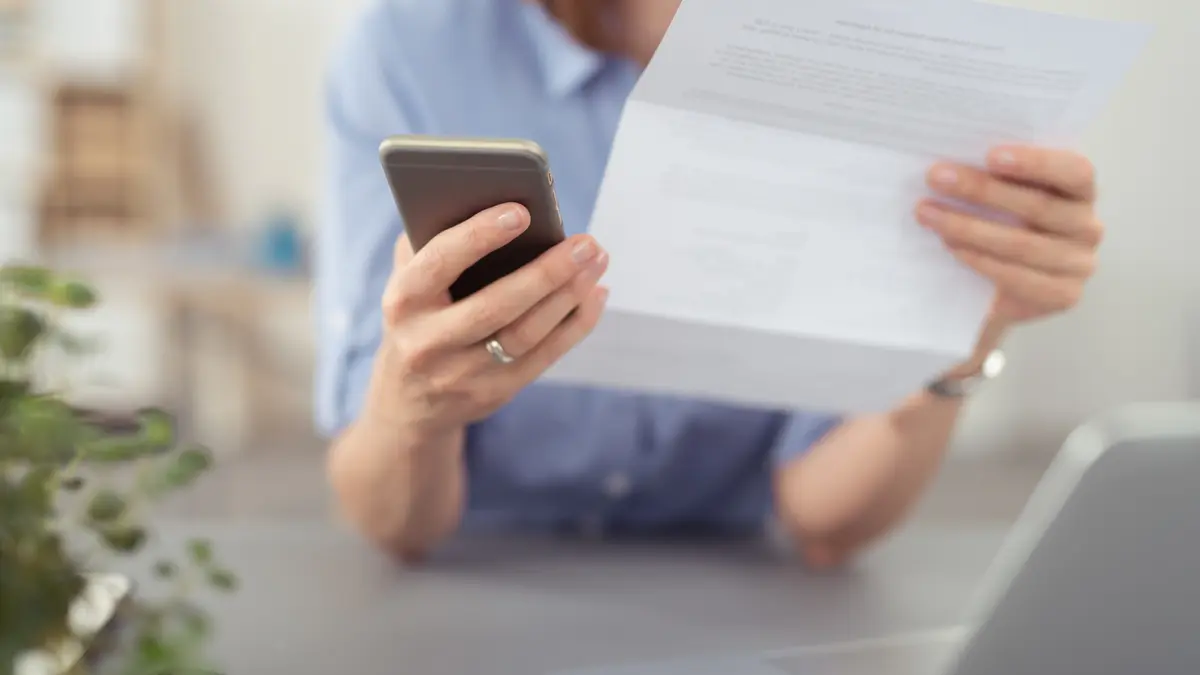 Frau liest Brief und wählt auf dem Telefon eine Nummer