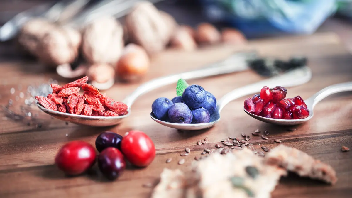 Goji Beeren, Acai Berren und andere sogenannte Superfoods liegen in einem Löffel auf einer hölzernen Arbeitsplatte