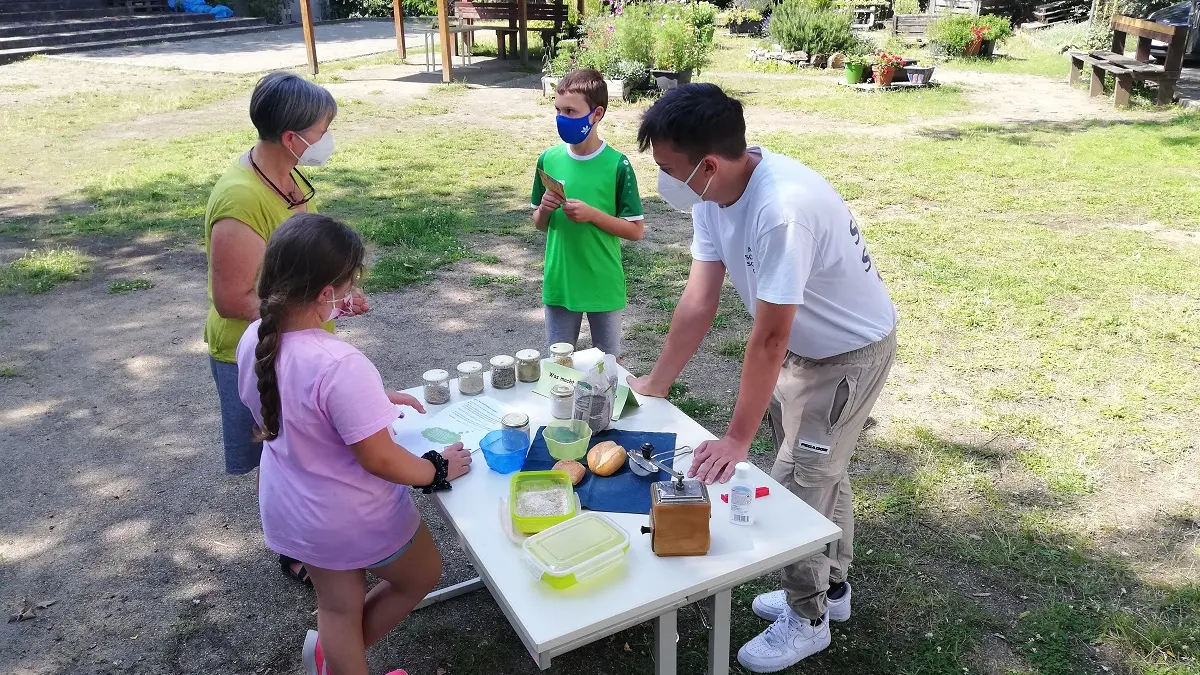 Drei Kinder und eine Erwachsene stehen an einem Tisch mit verschiedenen Materialien.