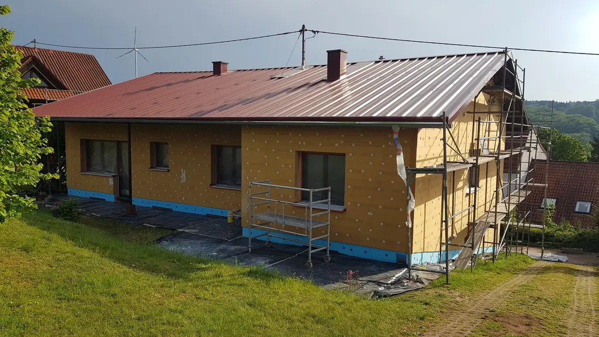 Ein einstöckiges Haus wird saniert. Wärmedämmplatten werden außen am Haus angebracht. Verschiedene Baugerüste sind zu sehen.