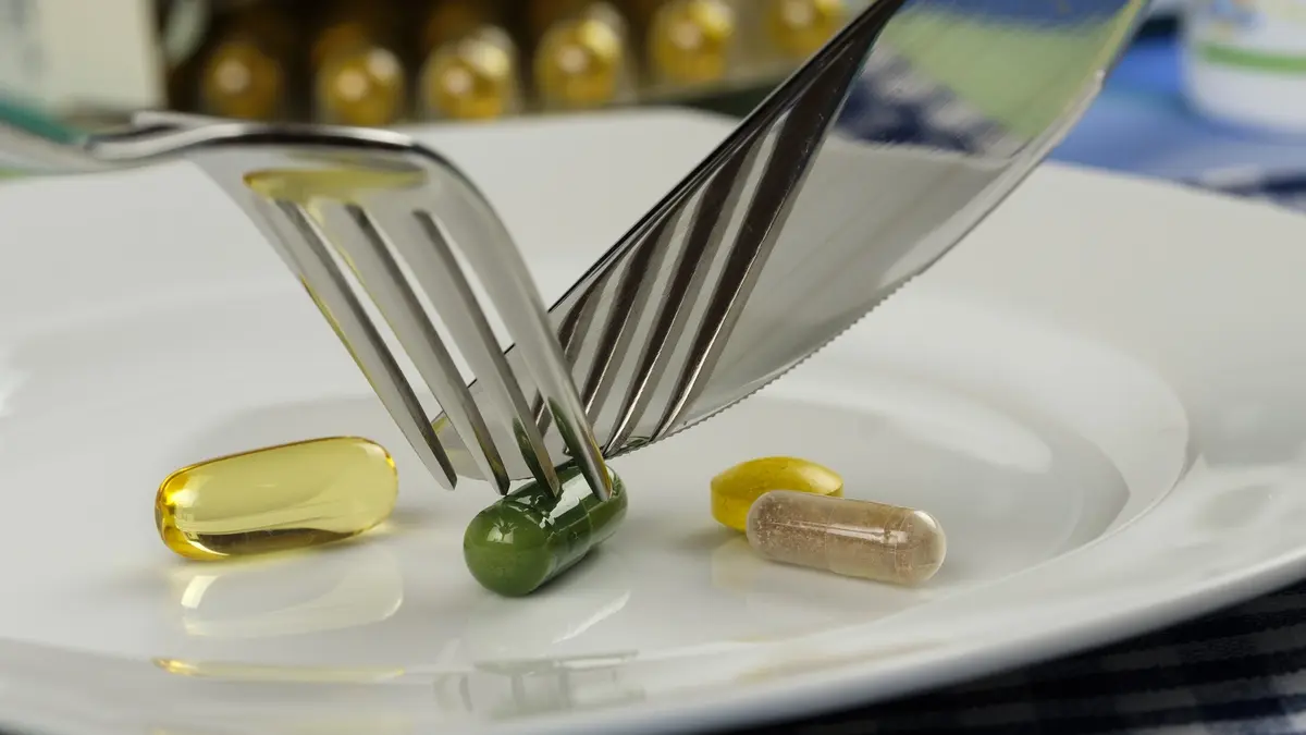 Jemand zerschneidet Schlankheits-Tabletten mit Messer und Gabel auf einem Teller