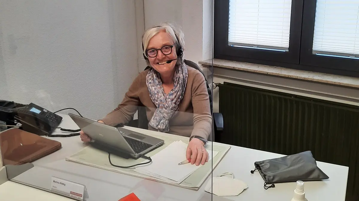 Eine Frau sitzt an einem Bürotisch und lächelt in die Kamera.