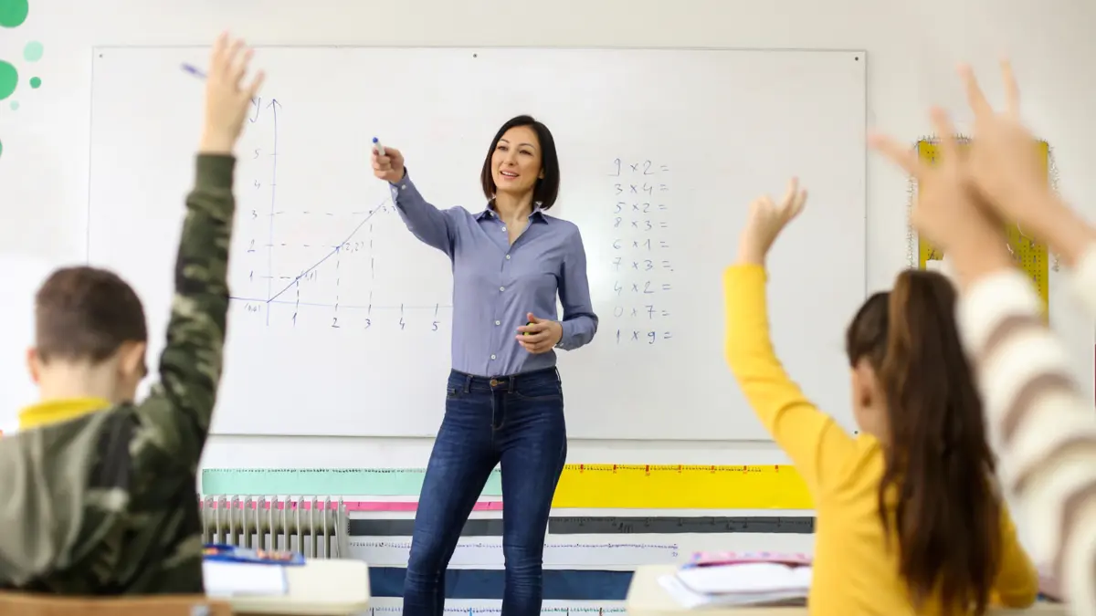 Lehrerin steht vor einer Klasse. Die Schulkinder zeigen auf.