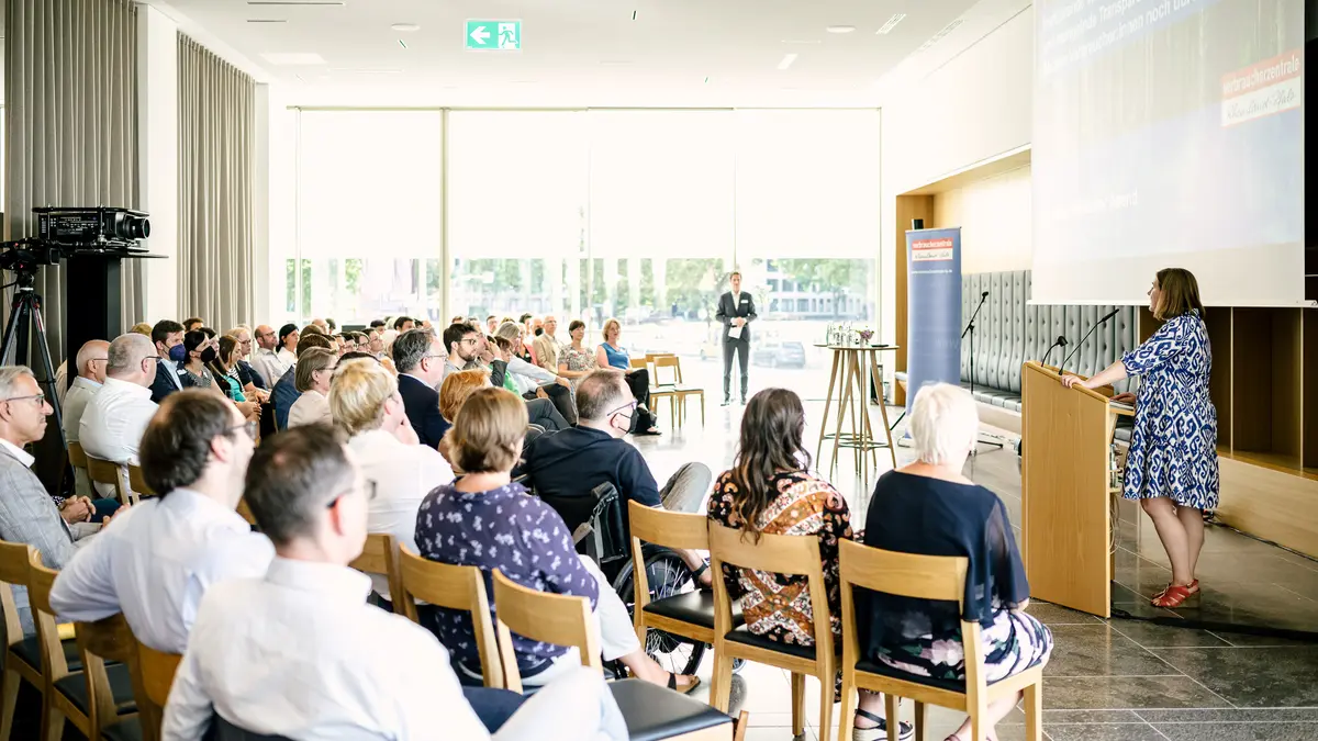 Eine Frau steht am Rednerpult und links von ihr sieht man das Publikum im Saal.