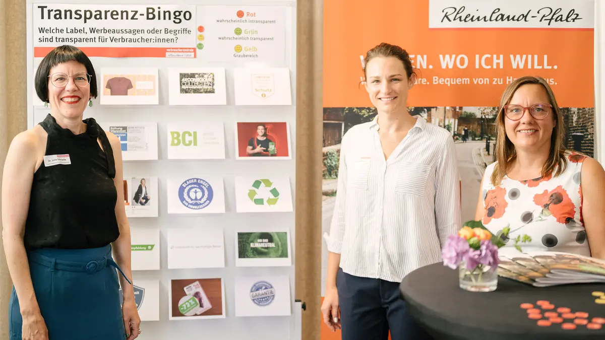 Drei Frauen stehen vor einem interaktivem Spiel und lächeln in die Kamera.