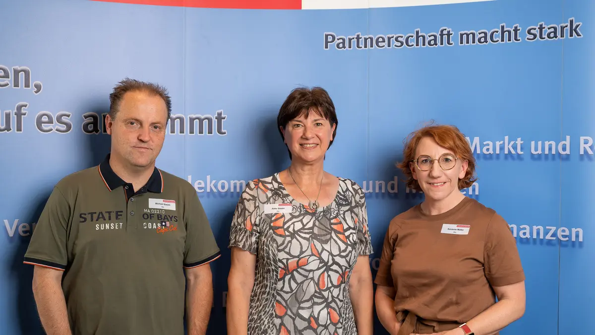 Drei Personen stehen vor einer Fotowand.