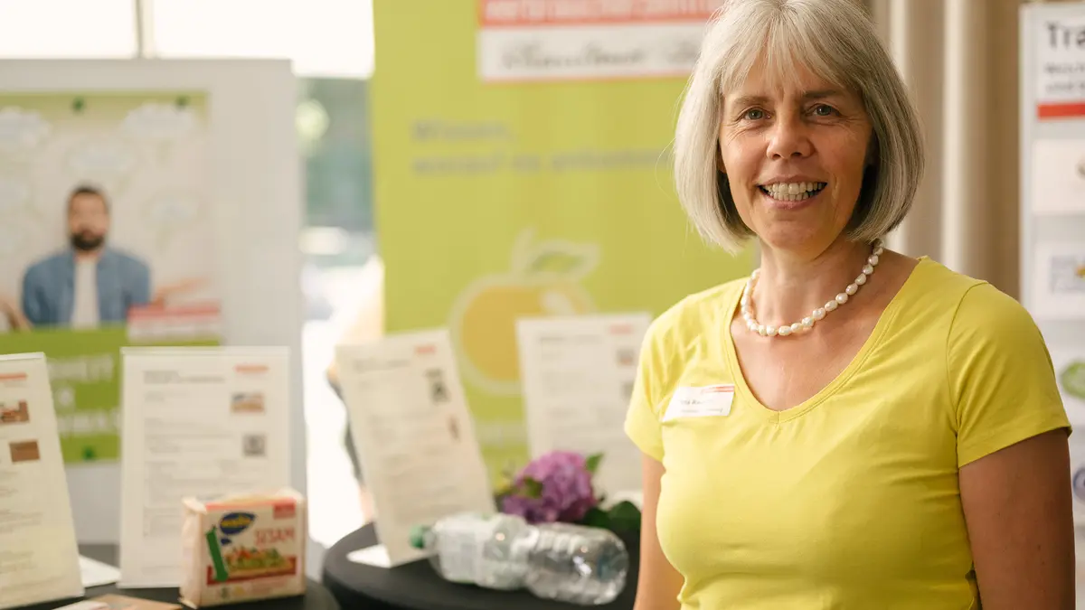 Eine Frau steht lächelnd vor einem Messestand.